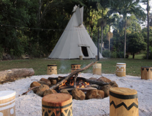 Firepit on white sand with timer seats and teepee in the background